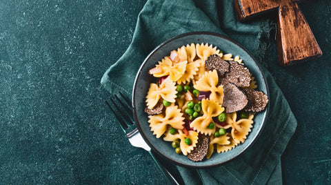 Una ciotola di pasta farfalle con piselli e fette di tartufi neri